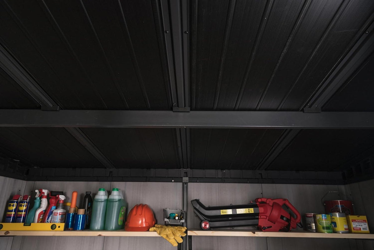 Interior view of shed ceiling with black support beams and a top shelf holding bottles, a helmet and tools.