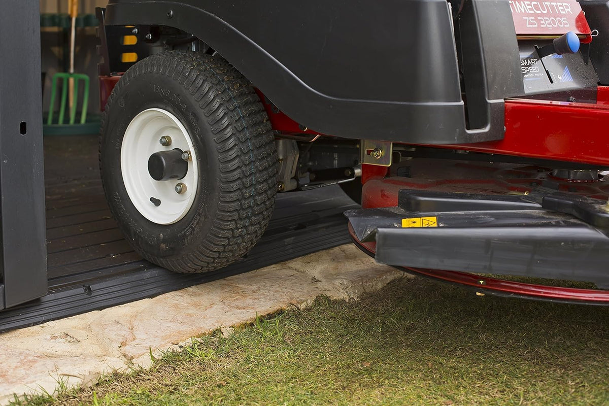 Close-up of a lawnmower wheel and deck at the shed threshold, showing the low ramp and floor.