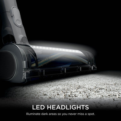 Low-angle close-up of the vacuum brushroll with LED headlights casting light across the floor.