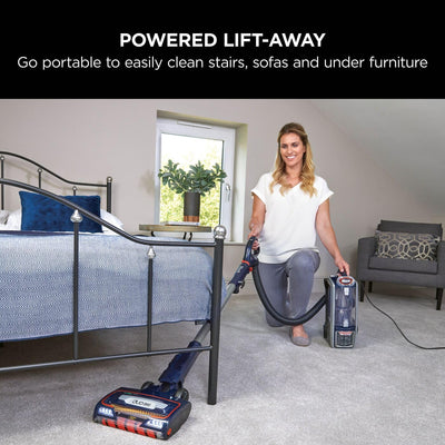 Woman using the Lift-Away portable canister and hose to vacuum a bedroom floor beside a bed.