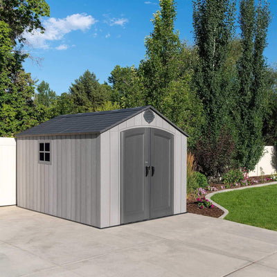 Shed gable and roof with circular vent set against tall backyard trees and a clear blue sky.